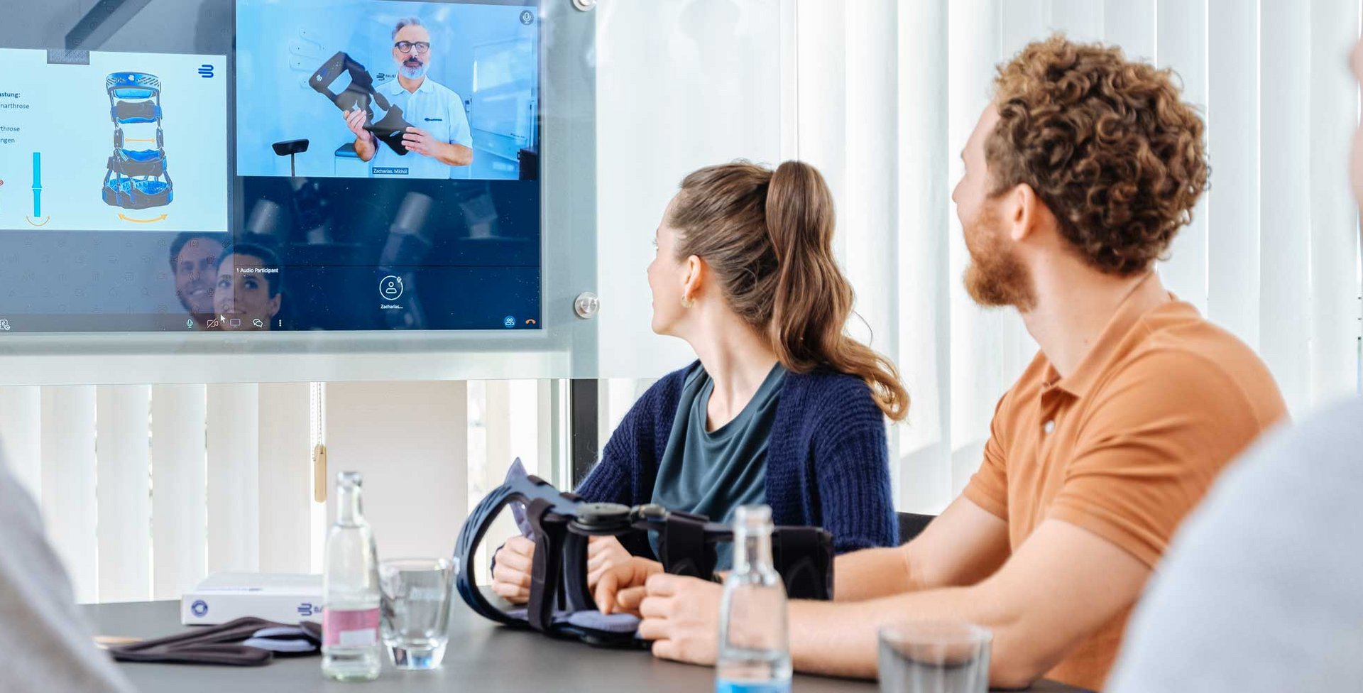 Mehrere Personen sitzen in einem Schulungs- oder Webinarraum und schauen auf eine große Projektionsfläche bzw. Leinwand, auf der Inhalte präsentiert werden. Im Vordergrund sieht man Köpfe und Schulungsteilnehmer.