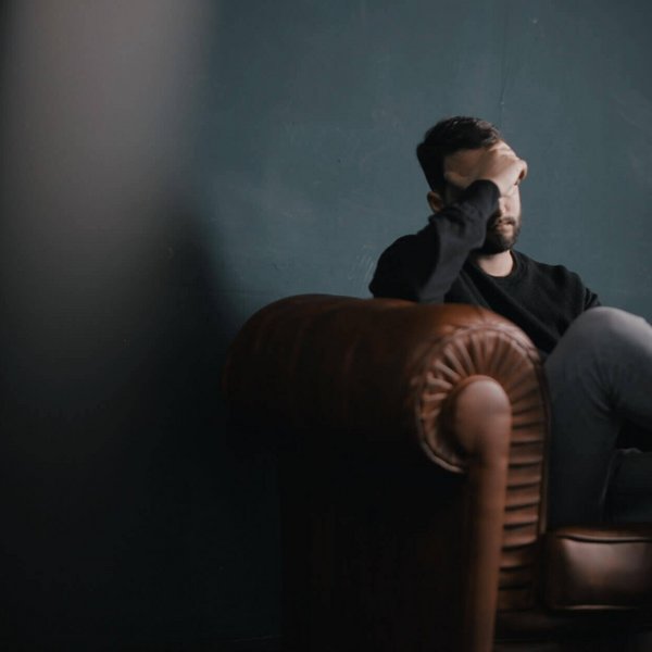 Das Bild zeigt einen gestressten Mann, der auf einer Couch sitzt. Ein Grund für Stress können Rückenschmerzen sein.