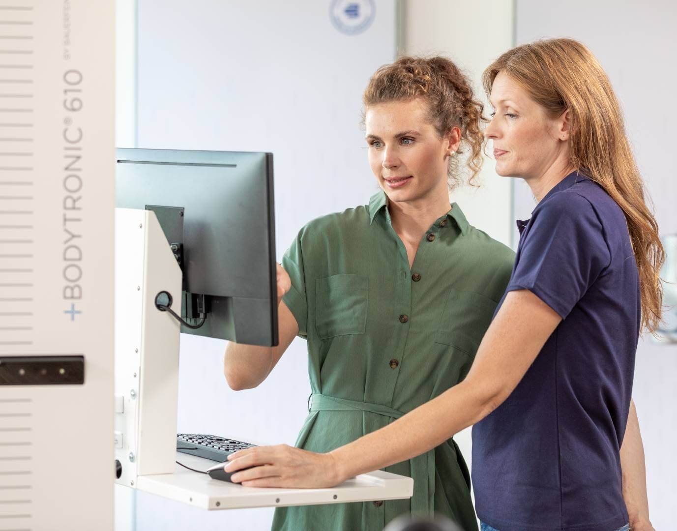 Zwei Frauen arbeiten mit der digitalen Messtechnik Bodytronic 610 von Bauerfeind, eine Frau zeigt auf den Bildschirm, während die andere aufmerksam zusieht, in einem modernen Messraum.