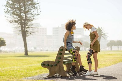 Das Bild zeigt zwei Frauen im Gespräch bei einer Parkbank. Beide tragen Knieorthesen von Bauerfeind zur Stabilisierung ihres verletzten Knies.
